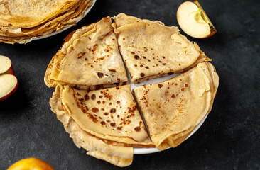 Thin homemade pancakes with apples on a stone background