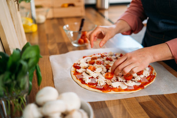 Obraz na płótnie Canvas Woman's hands adding cherry tomatoes to a traditional margarita pizza. Preparation of a Original Italian pizza