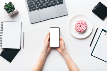 Female hands holding cellphone with blank screen and morning donut