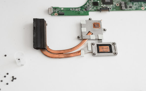 different parts of the laptop are on the white table disassembled. Mother board and cooling system are separated