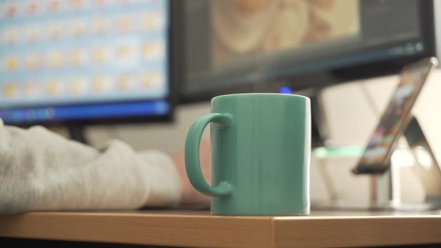 Photographer retouching photos, working at home with a cup of steaming coffee