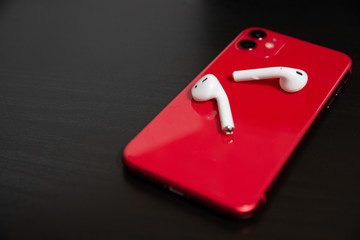 Red smartphone with wireless headphones on a black wooden background