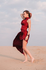 Fototapeta na wymiar girl in the desert at sunset in a red dress developing in the wind