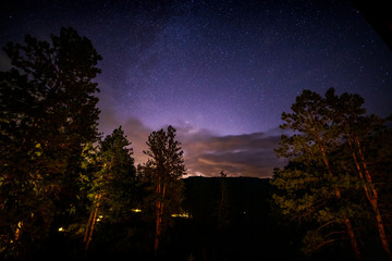 A starry sky over the mountainous region of Bailey, Colorado with the lights of Denver, Colorado in the background.