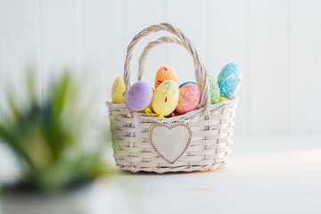 Multi-colored Easter eggs in a basket on a white wooden background