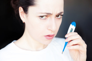 Young woman holding medicine equipment thermometer isolated on dark black background. Ill girl...