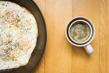 cup of tea with fried eggs in a pan on a wood background