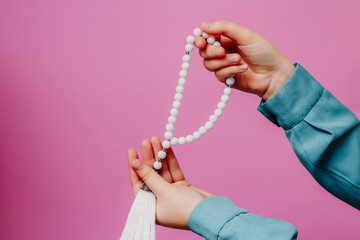 Muslim rosary in hands. On a pink background