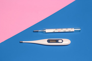 two thermometers, one mercury and the other electronic on a pink and blue background