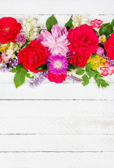 flower arrangement border of different wild and garden flowers of roses, peonies and jasmine on a white wooden background with copy space, top view