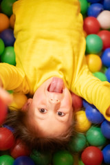 Fototapeta na wymiar Little girl in a ball pit smiling at the camera, raising hands, having fun at the children play center
