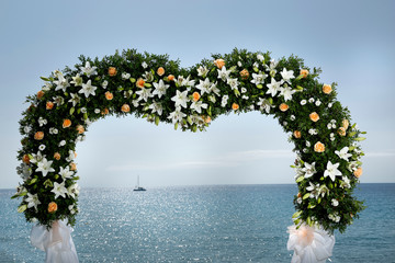 Decorazione floreale a forma di cuore di altare per una cerimonia al mare, sfondo cielo mere e una barca 