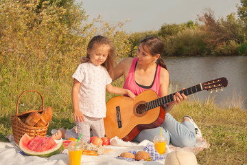 Mom and daughter play the guitar while sitting on the grass during a picnic in the park