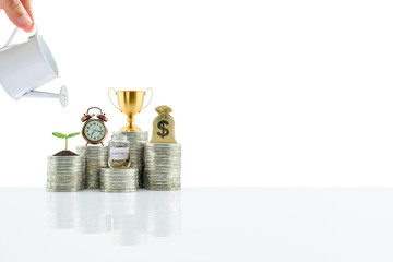 Water is poured from a watering can on small tree and stacks of coins with saving jar, a dollar bag