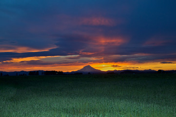 Distant view of Mount Shasta with orange glow in clouds at sunset, view west from near McArthur,...