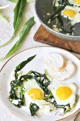 fried eggs with wild garlic as a shakshuka. fried eggs in a frying pan under gray marble on a table. Keto diet dish