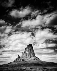A black and white view of Agathla, El Capitan as clouds flow above