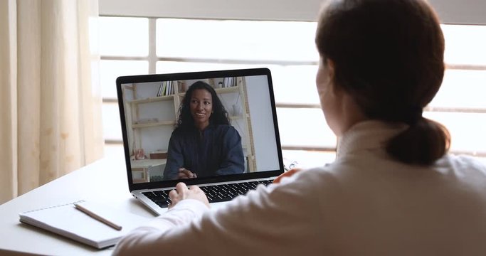Diverse business women video calling working from home office. Over shoulder laptop screen view of female recruiter, hr manager interviewing african candidate, consulting client in webcam virtual chat
