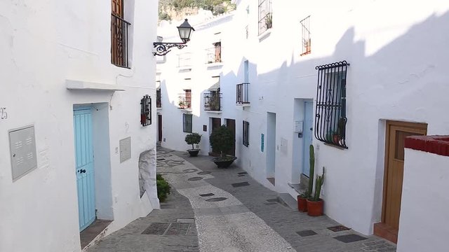 Picturesque narrow street with white houses , beautiful flowers and souvenir shop in village of Frigiliana, in south of Spain.