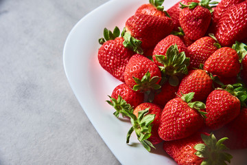 Fresas frescas sobre plato blanco y mesa de cemento o marmol gris