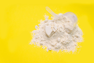Measuring cup from a white powder whey protein on a yellow background