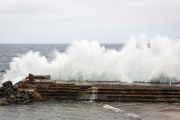 Ocean waves splashing against breakwater in Bajamar natural pool area on cloudy day. Rough sea in...