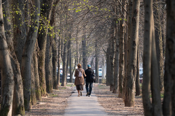 man and woman spend time outdoors. cute couple in caps walk along the alley between the trees on a spring day
