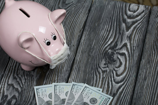 Ceramic piggy bank in pink. With a gauze bandage. In front of her are a few dollar bills. Savings during an epidemic. It stands on black painted boards.