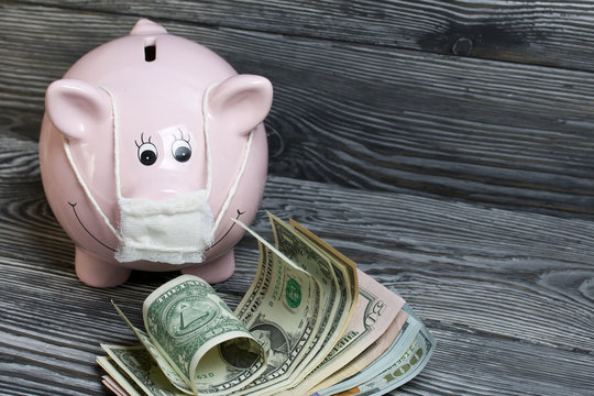 Ceramic piggy bank in pink. With a gauze bandage. In front of her are a few dollar bills. Savings during an epidemic. It stands on black painted boards.