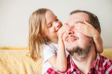 Little girl wishes dad happy father's day. Daughter hugs dad, closes his eyes with his hands