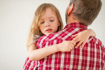 Little sad girl on dad's arms. Daughter hugs dad.