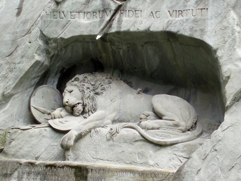 Monument "The Dying Lion" in Lucerne.Switzerland. High relief carved in a steep rock. The dying lion lies with its head resting on its right paw, resting on a shield with a picture of a lily. Helvetia
