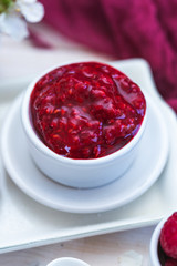 Raw raspberry jam in a white cup with raw raspberry rolls. Vegan food.