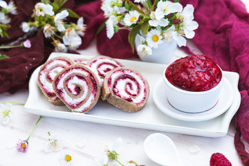 Vegan raw raspberry rolls with coconut flour on a white table with spring flowers and red silk. Vegan cookies with birch sugar on a white plate. Spring flowers. Daisies.