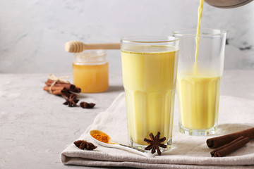 Ayurvedic golden turmeric latte milk in two glasses with curcuma powder, cinnamon and anise star on gray background, Closeup, Copy space