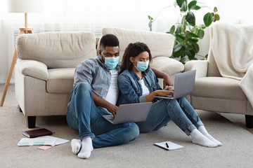 Fototapeta na wymiar Self-isolated couple working remotely on laptops at home, wearing medical masks
