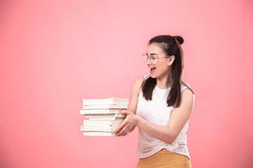 Portrait of a young woman with glasses on a pink background with books in her hands .