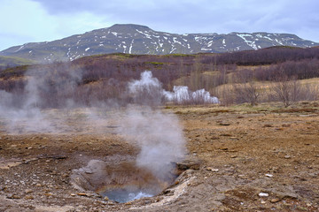 Steam pours out from the various mud puddles and vents all around Stokkur Geyser in Iceland and the surrounding landscape and mountains