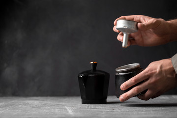 Fototapeta na wymiar Side view on male hands holding opening black geyser coffee maker on the grey background, horizontal format 