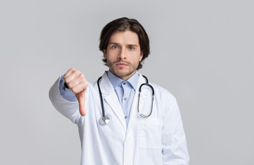 Fototapeta premium Portrait of serious confident young doctor showing thumb down gesture