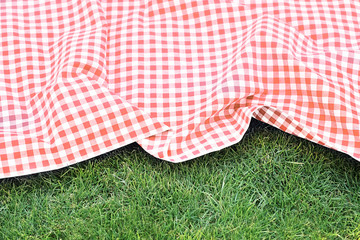 Red checkered picnic cloth on green grass background,empty space food advertisement backdrop.