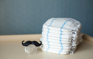 A mustache-shaped pacifier and a stack of baby diapers are on the dresser. Blue background.