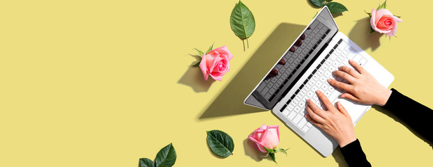 Fototapeta na wymiar Woman using her laptop with pink roses - flat lay