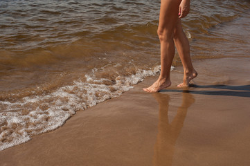 feet of a girl on a sandy beach by the water