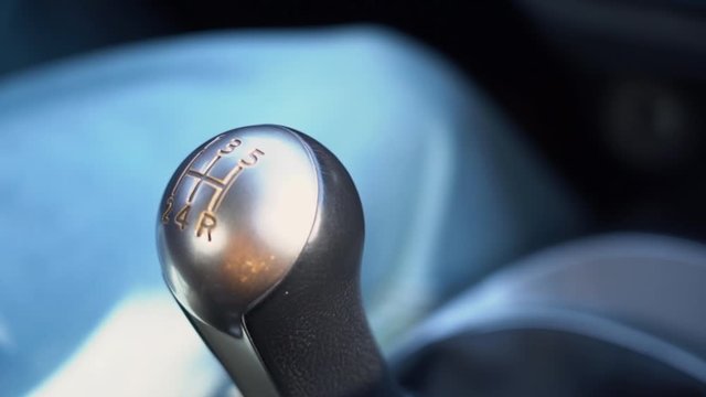 View of the gray and silver lever of a manual gearbox of a car with gear numbers c9lose up in sunny day in a driving car slow motion.