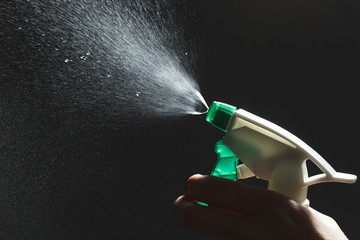 Close-up view of human hand and antiseptic spray bottle on dark background. Control Epidemic...