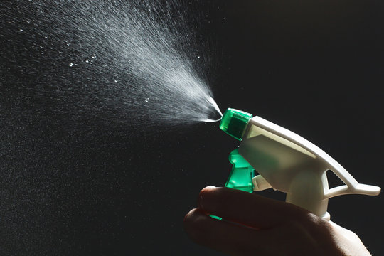 Close-up view of human hand and antiseptic spray bottle on dark background. Control Epidemic Prevention measures of coronavirus.
