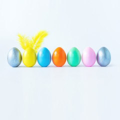 Fototapeta na wymiar Top view of an easter composition of painted eggs in bright juicy colors on a white background with feather rabbit ears. Vacation concept, flat design, minimalism.