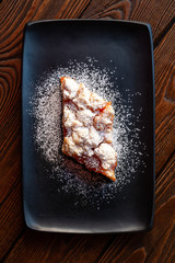 Homemade apricot pie. Top view slice of rustic hot sweet cake sprinkle with powdered sugar in a black plate on a wooden background. Natural organic food. Selective soft focus.