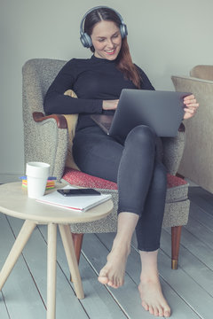 Happy young woman is siting in a stylish apartment. She is fulfilling her free time at home with digital entertainment. Time for a break from exhausting  home office or distance education. 